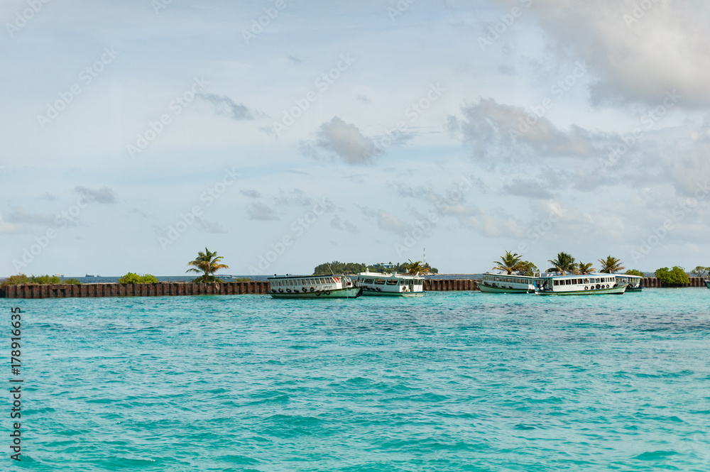 Obraz premium Tropical wharf with boats in Maldives in Indian Ocean. Ships on the water. Piece of paradise on the Earth. Good choice for vacation. Beautiful view for wallpaper.