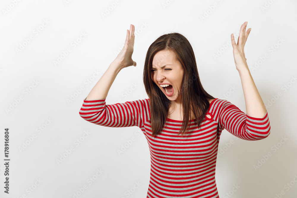 Pretty European young angry brown-haired woman with healthy clean skin, dressed in casual red and grey clothes, screaming, swearing and waving her arms, on a white background. Emotions concept.
