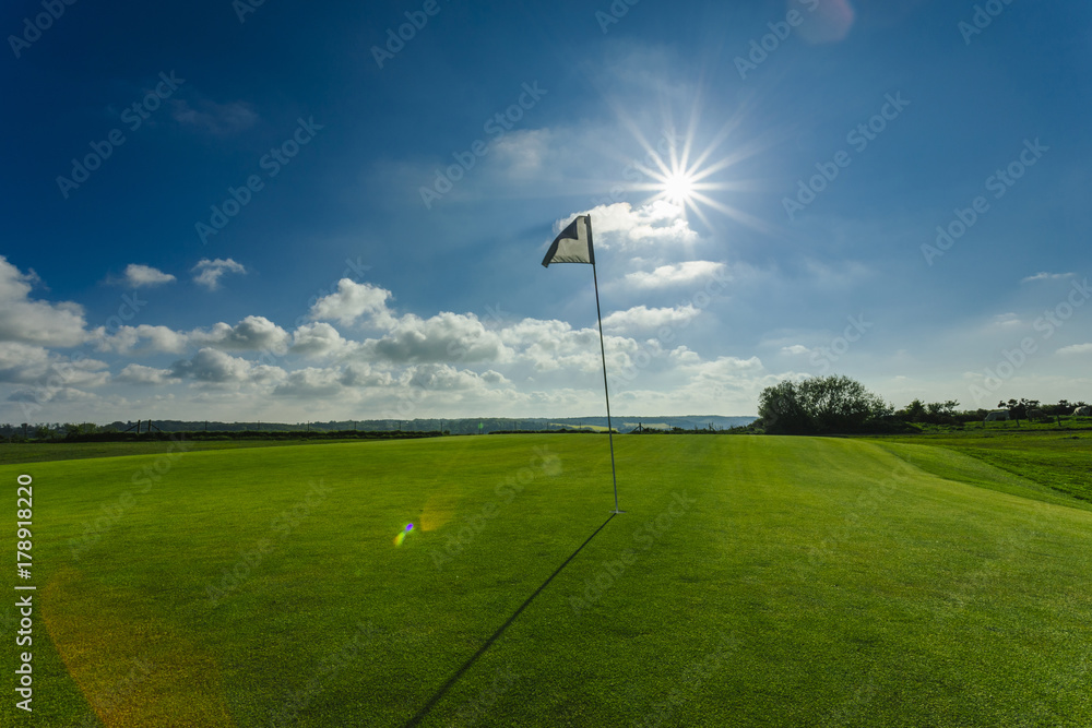 View of a green golf course, hole and flag on a bright sunny day. Sport, relax, recreation and leisure concept. Summer landscape with sunbeams View of a green golf course, hole and flag on a bright sunny day. Sport, relax, recreation and leisure concept. Summer landscape with sunbeams