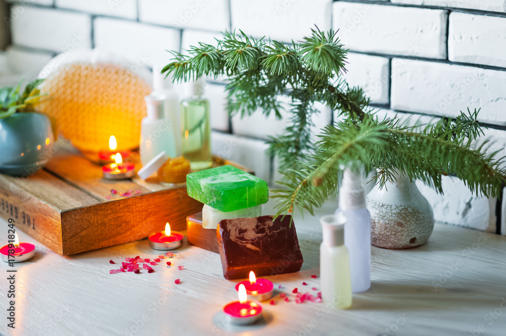 Spa accessories. Sprigs of a Christmas tree, many multi-colored pieces of soap, many different shapes of bottles for a bathroom. Body scrub. Light brick and white wooden as a background Spa accessories. Sprigs of a Christmas tree, many multi-colored pieces of soap, many different shapes of bottles for a bathroom. Body scrub. Light brick and white wooden as a background