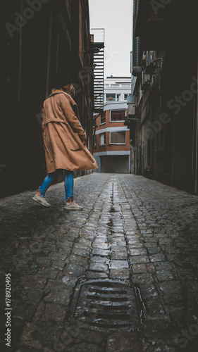 Lifestyle full portrait of young attractive fashionable Caucasian female in a coat walking in the narrow street in Europe. Vertical photo © supamotion