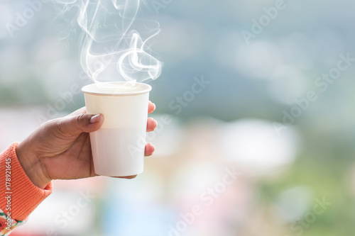 Female hand in mittens holding cup with hot tea or coffee. Tea break. Winter and touring time concept