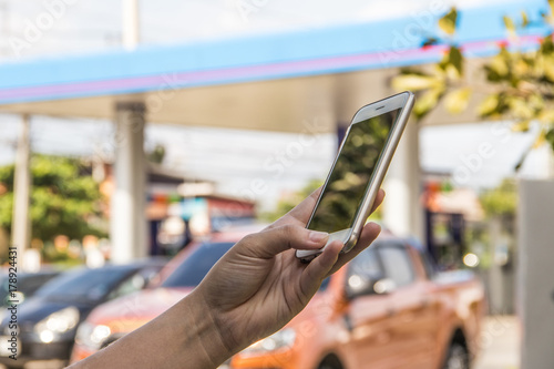 Hand hold mobile on front with blurred gas station background