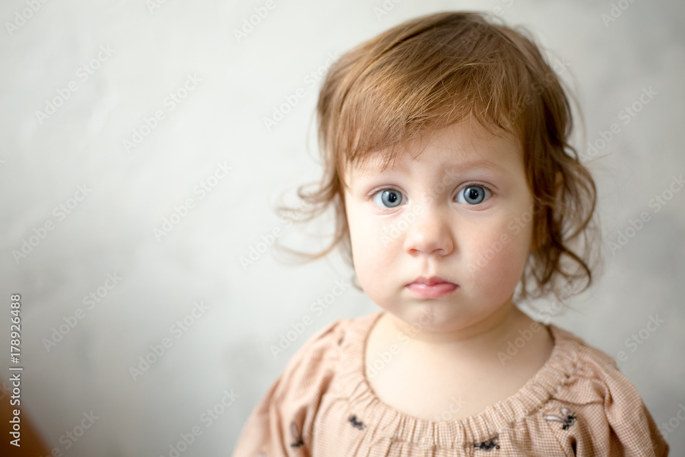 Portrait of little girl on gray background. Full cheeks, thick blond hair. Sweet girl with curly hair against a textured wall. The girl in pajamas.