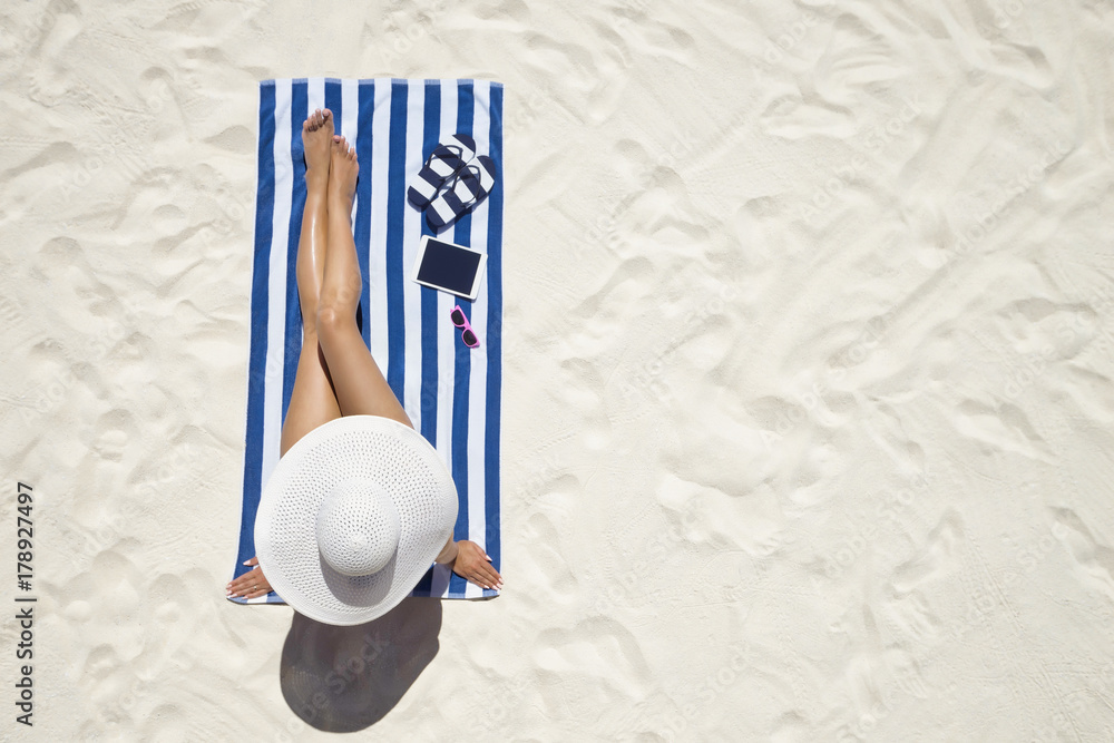 Summer holiday fashion concept - tanning woman wearing sun hat at the beach on a white sand shot from above - obrazy, fototapety, plakaty 