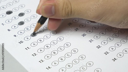 Student hand testing doing examination test with standardized test form and answers bubbled. Student filling out answers.