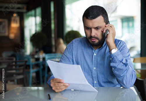 Worried man using phone and looking documents