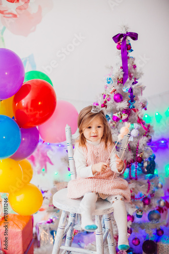 Little girl in pink dress plays in the room with pink Christmas tree