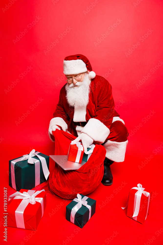 Holly jolly x mas noel time! Funny santa in headwear, costume, black belt, shoes, white gloves fills sack with a lot of gifts for kids, with ribbon tapes bows, digital devices Holly jolly x mas noel time! Funny santa in headwear, costume, black belt, shoes, white gloves fills sack with a lot of gifts for kids, with ribbon tapes bows, digital devices