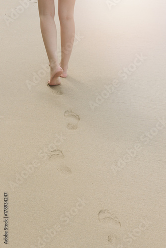 back view of woman walking on sand beach leaving footprints in the sand. 