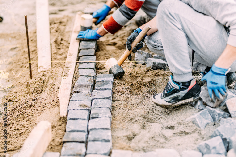 Industrial construction worker paving road with granite cobblestone using sand and rubber hammer Industrial construction worker paving road with granite cobblestone using sand and rubber hammer