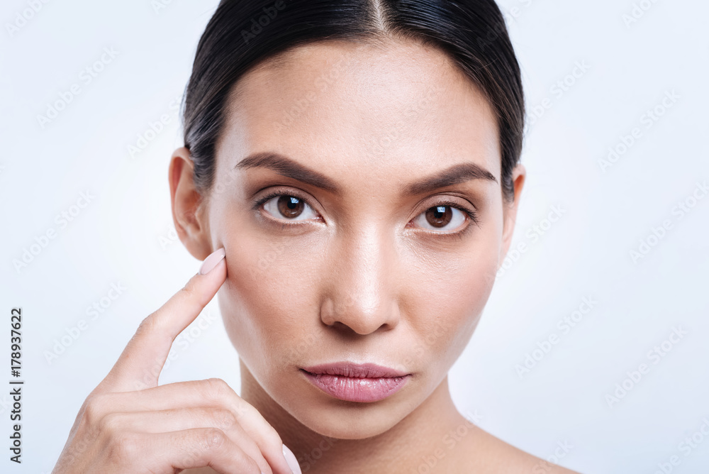 Close up of young brunette touching her cheekbone with finger Close up of young brunette touching her cheekbone with finger