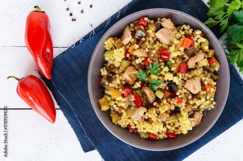 Light healthy dietary salad with couscous, vegetables (zucchini, eggplant, carrots, sweet peppers, onions), chicken pieces on a white wooden background. photo