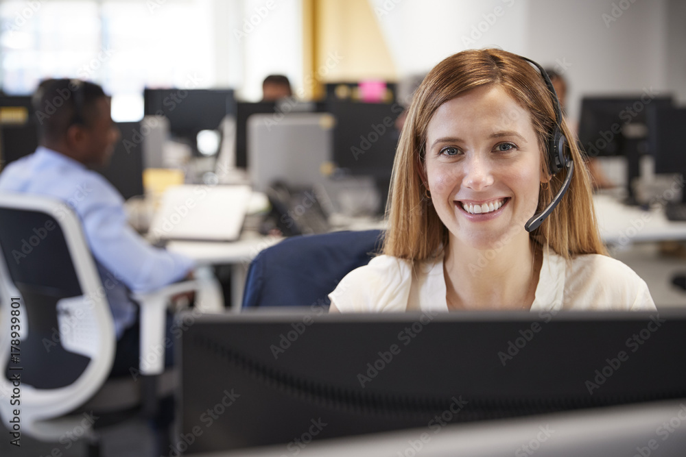 Obraz premium Young woman working at computer with headset in busy office