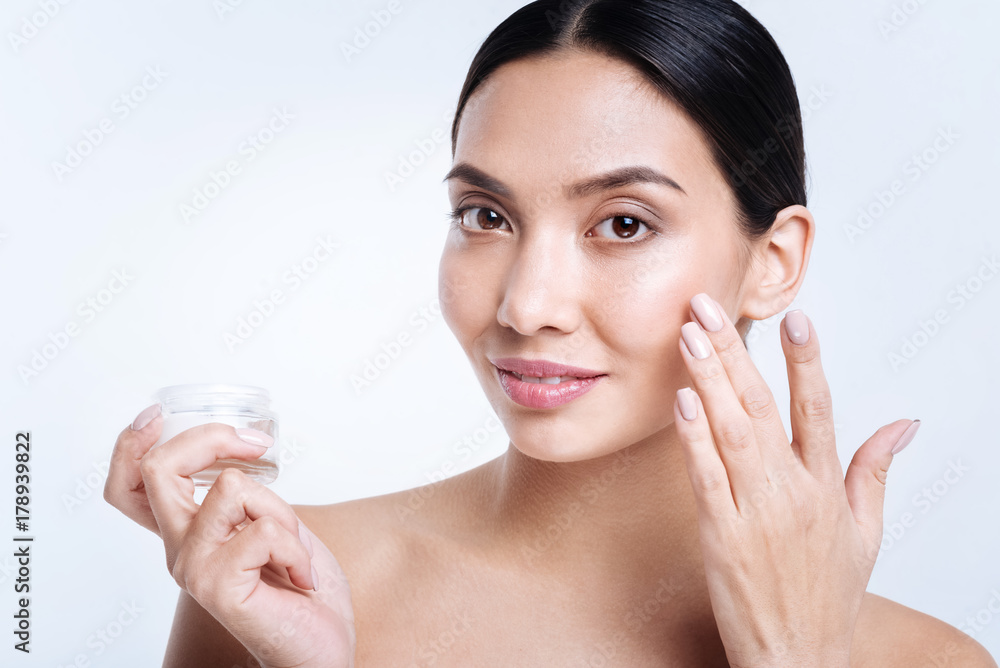 Close up of pleasant woman applying cream to her face Close up of pleasant woman applying cream to her face