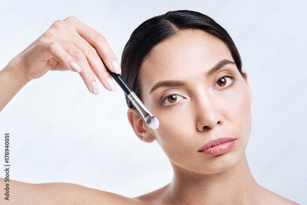 Pretty brunette holding makeup brush near her face Pretty brunette holding makeup brush near her face