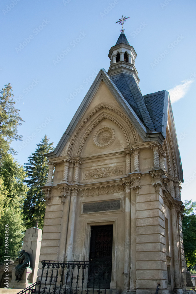 gray richly carved and decorated tombstone surrounded by greenery and warm sunshine shining from behind the trees