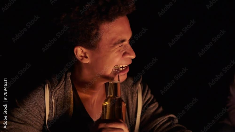 Attractive african american opening a beer bottle with teeth and giving it to his girlfriend while sitting by the bonfire late at night Attractive african american opening a beer bottle with teeth and giving it to his girlfriend while sitting by the bonfire late at night