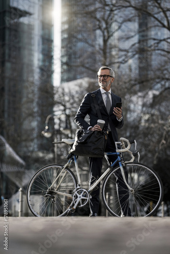 Fototapeta Naklejka Na Ścianę i Meble -  Grey-haired businessman with bicycle and coffee to go in the city