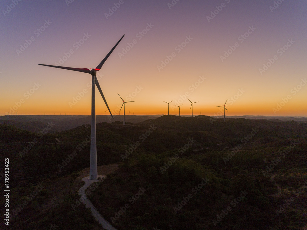 Obraz premium Aerial panoramic Wind farm turbines silhouette at sunset. Clean renewable energy power generating windmills. Algarve countryside.