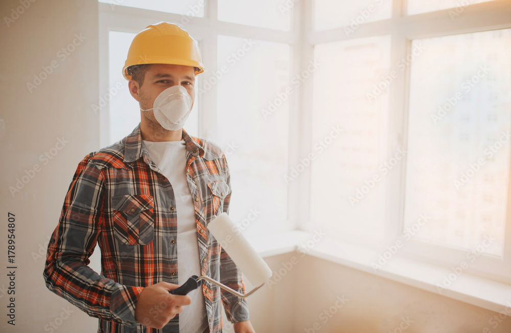 The builder works at the construction site and measures the ceiling. A worker in an orange helmet and a paint roller paints the wall. The builder works at the construction site and measures the ceiling. A worker in an orange helmet and a paint roller paints the wall.