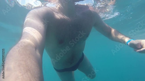 Unrecognizable man swimming in sea with camera is in hand. Close up of male body under water. Slow motion