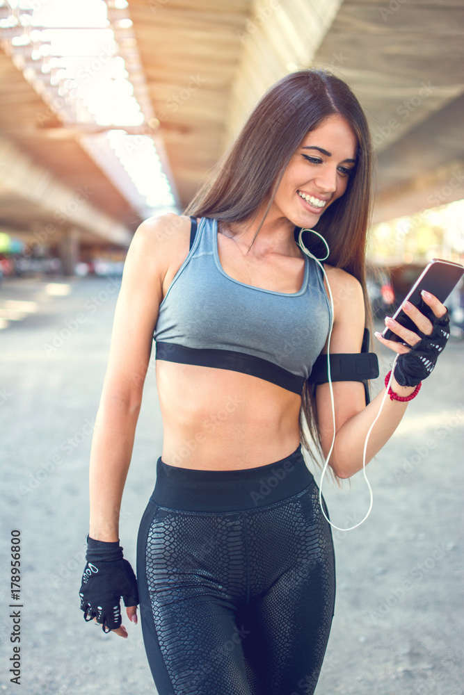 Smiling sporty girl using phone after sports training outdoors.