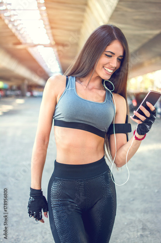 Smiling sporty girl using phone after sports training outdoors.