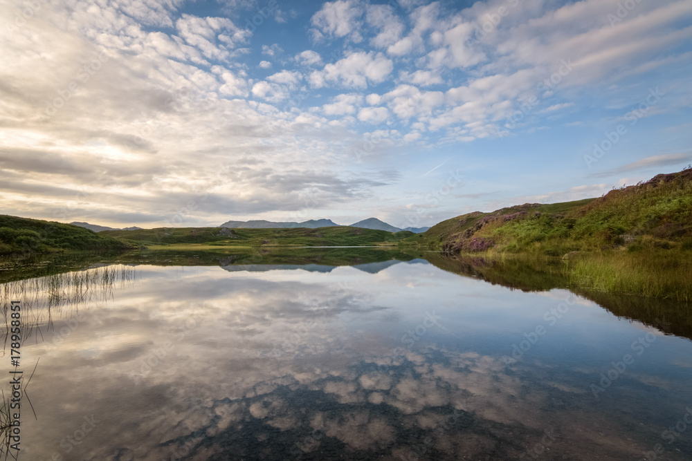 Sharp reflection of the warm colored clouds in the water of tarn Beacon Lake District mountain background