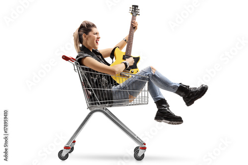 Punk girl sitting inside a shopping cart and playing an electric guitar