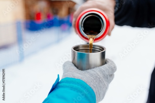 Woman pours hot tea or coffee from metal thermos
