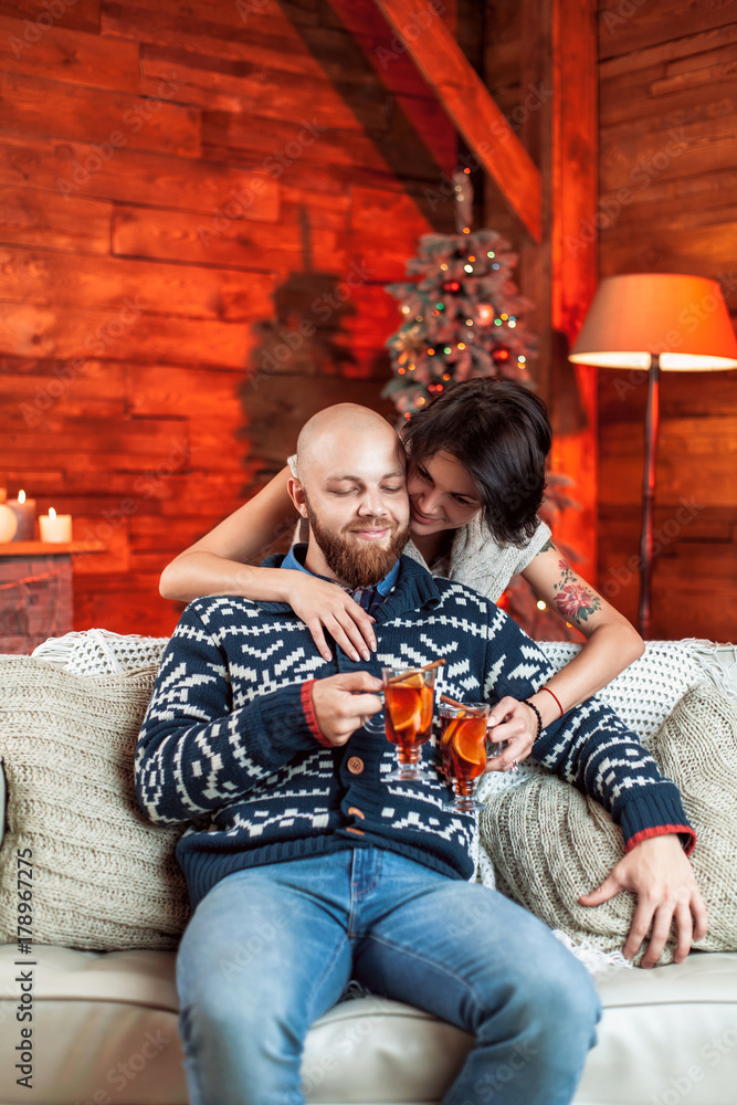 Beautiful couple sitting on the couch and holding a glass of mulled wine in a decorated festive interior with a Christmas tree. Concept of a family celebration, new year's eve