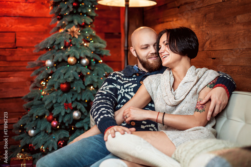 Beautiful couple sitting on the couch embrace in a decorated festive interior with a Christmas tree. The concept of a family celebration, new year's eve