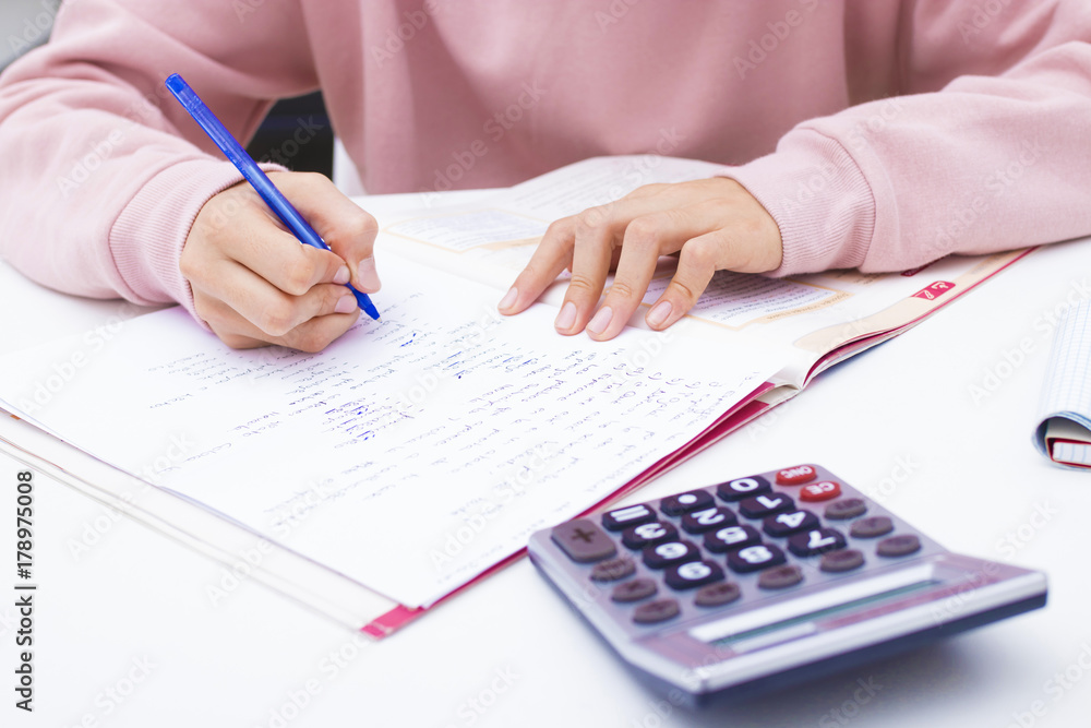 student hand writing with calculator at home or school