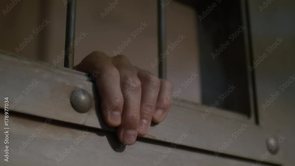 MAN'S HAND BETWEEN THE BARS OF A CELL DOOR, ECU IN 4K. MAN'S HAND BETWEEN THE BARS OF A CELL DOOR, ECU IN 4K.