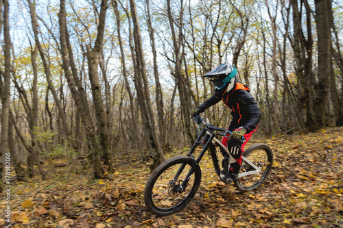 a young rider driving a mountain bike rides at speed downhill in the autumn forest.