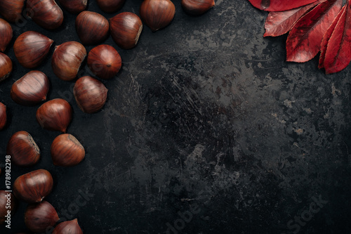 Tasty chestnuts on dark black rustic background. Pile of fresh chestnuts ready to roast shot over black antique background. Top view, copy space.