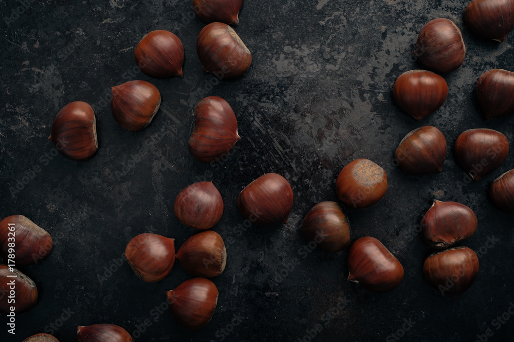 Fresh chestnuts on dark black rustic background. Pile of fresh chestnuts ready to roast shot over black antique background. Top view. Fresh chestnuts on dark black rustic background. Pile of fresh chestnuts ready to roast shot over black antique background. Top view.