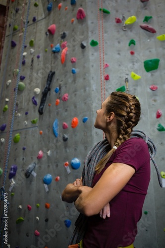 Athlete with rope looking up while standing by climbing wall in