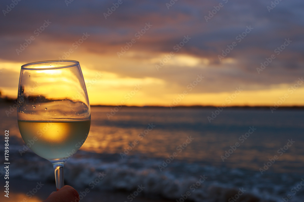 Female hand with a glass of white wine on the background of a beautiful sunset.  Travel vacations concept.