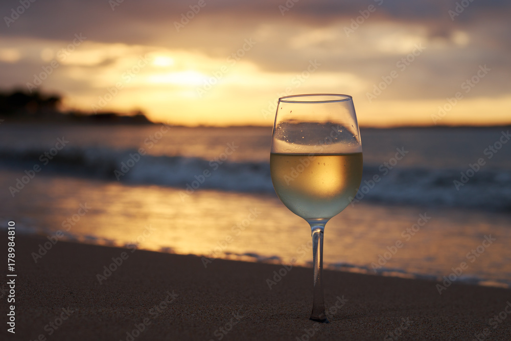 A glass of white wine on the beach at sunset. Travel vacations concept. A glass of white wine on the beach at sunset. Travel vacations concept.