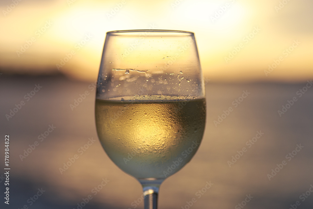 Wineglass of white wine at sunset dramatic sky background. Closeup. Travel vacations concept.
