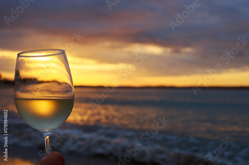 Female hand with a glass of white wine on the background of a beautiful sunset. Travel vacations concept.