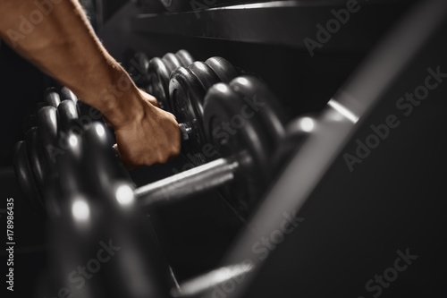 Dumbbell. Close-up man grabs a heavy dumbbell in the gym with his hand. Concept lifting, fitness.