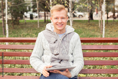 Young blond man sitting and listening music with earphones and tablet, lifestyle concept