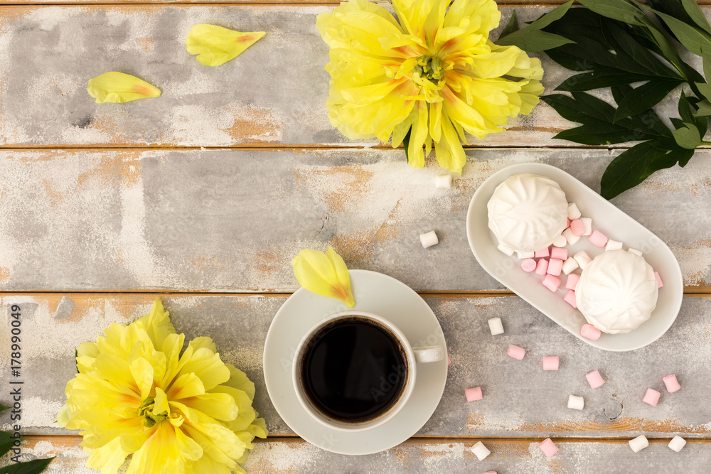 Morning coffee, marshmallows and beautiful yellow peony flowers on light table top view in flat lay style. Cozy breakfast on Mother or Woman day.