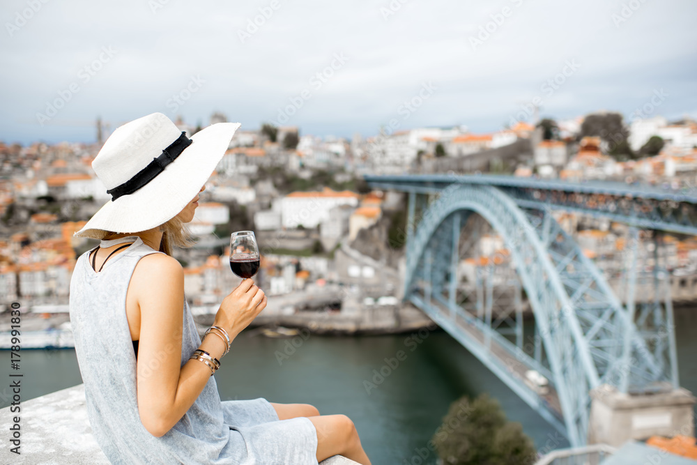 Young woman tourist sitting with glass of Porto wine on the terrace with great cityscape view on Porto city in Portugal