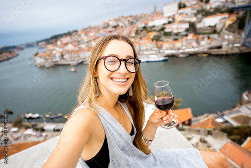 Portrait of a young and happy woman enjoying Porto wine, sitting on the terrace with beautiful cityscape view in Porto, Portugal