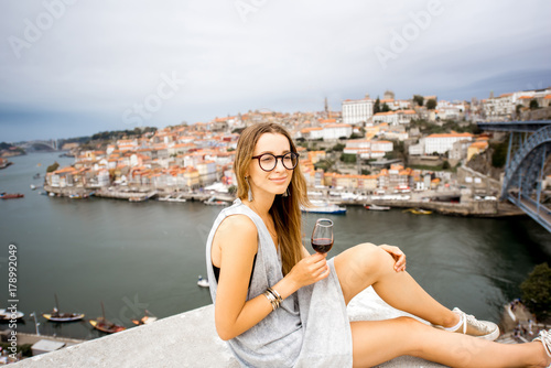 Portrait of a young and happy woman enjoying Porto wine, sitting on the terrace with beautiful cityscape view in Porto, Portugal © rh2010