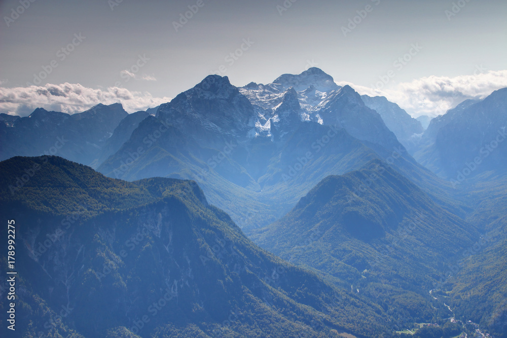 Snowy Triglav and Rjavina peaks from the north with forested Jerebikovec peak and deep Vrata, Kot and Sava Valley in a sunny autumn day, Triglav National Park, Julian Alps, Slovenia, Europe